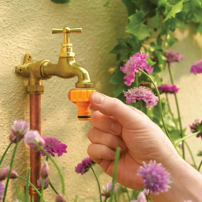 Hand turning on a gold garden faucet with purple flowers in the background